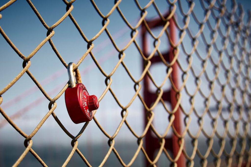 Red Padlock Hanging on a Chain Link Fence